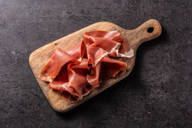 Jamón serrano español con aceitunas y palitos de pan sobre fondo negro