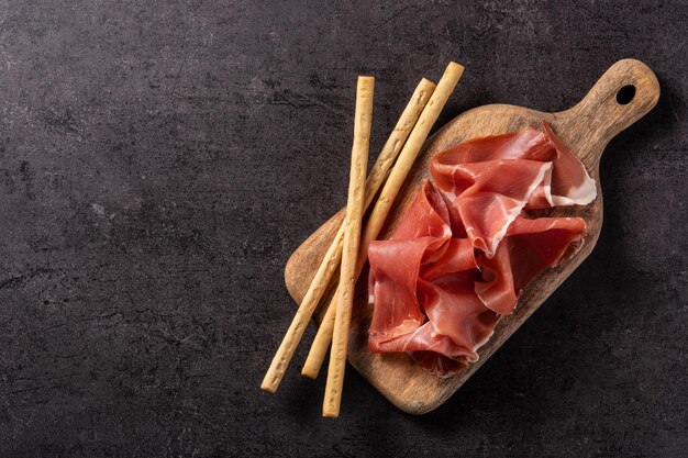 Jamón serrano español con aceitunas y palitos de pan sobre fondo negro