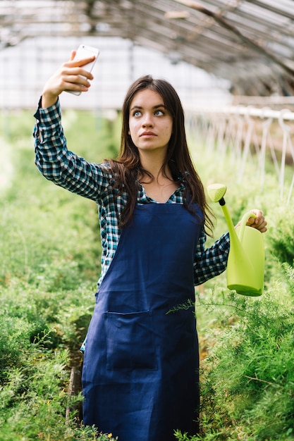 Foto gratuita jardinera joven con teléfono en el invernadero