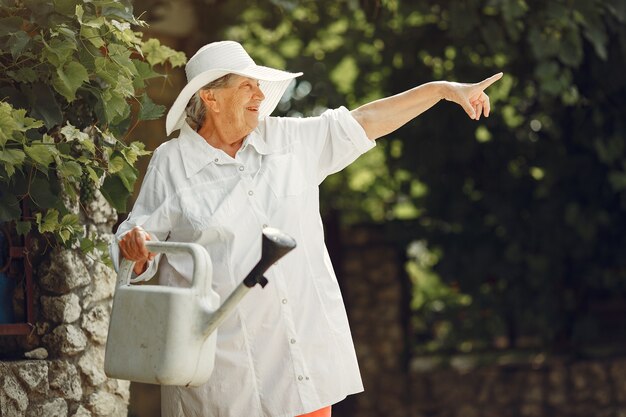 Jardinería en verano. Mujer regando las flores con una regadera. Anciana con sombrero.