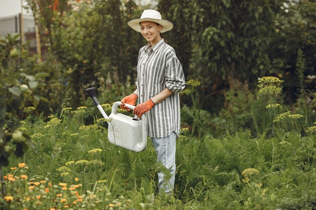 Jardinería en verano. Mujer regando las flores con una regadera. Chica con sombrero.