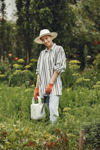 Jardinería en verano. Mujer regando las flores con una regadera. Chica con sombrero.