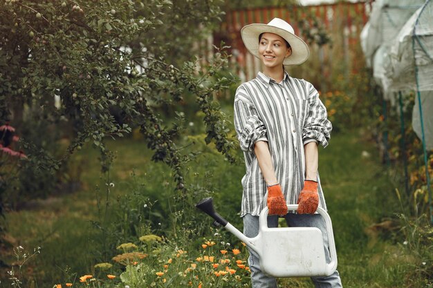 Jardinería en verano. Mujer regando las flores con una regadera. Chica con sombrero.