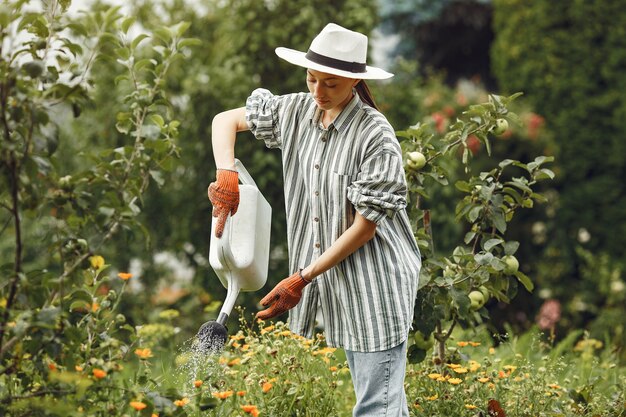 Jardinería en verano. Mujer regando las flores con una regadera. Chica con sombrero.