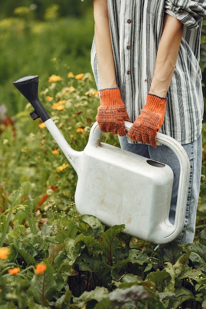 Foto gratuita jardinería en verano. mujer regando las flores con una regadera. chica con sombrero.