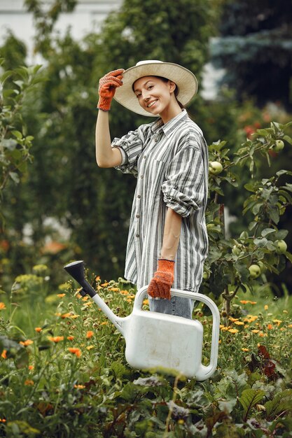 Jardinería en verano. Mujer regando las flores con una regadera. Chica con sombrero.