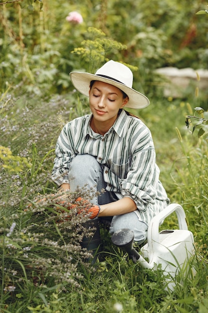 Jardinería en verano. Mujer regando las flores con una regadera. Chica con sombrero.