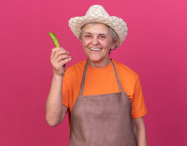 Jardinero anciano sonriente con sombrero de jardinería sosteniendo pimiento picante roto