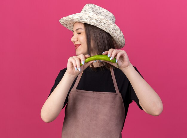 Jardinero femenino bastante caucásico disgustado vistiendo sombrero de jardinería sosteniendo pimiento picante