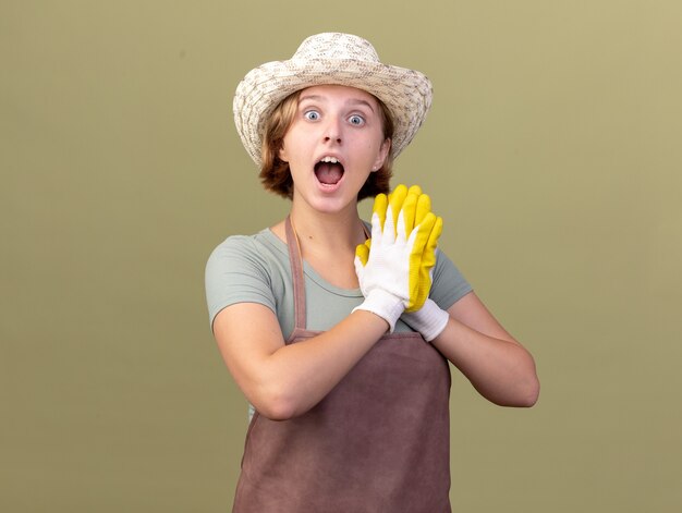 Jardinero femenino eslavo joven emocionado con sombrero de jardinería y guantes tomados de la mano juntos en verde oliva