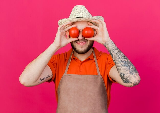 Jardinero macho disgustado con sombrero de jardinería sostiene y cierra los ojos con tomates