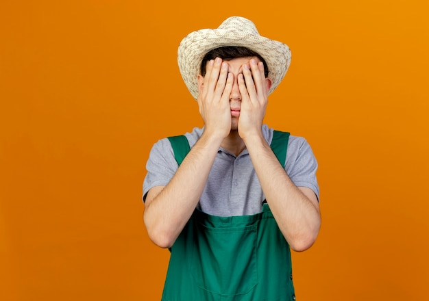 Jardinero macho joven decepcionado con sombrero de jardinería pone las manos en la cara