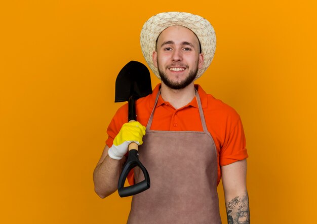 Jardinero macho sonriente vistiendo guantes y gorro de jardinería tiene pala