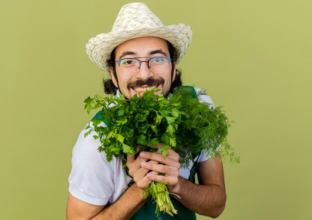 Jardinero masculino alegre en gafas ópticas con sombrero de jardinería tiene hinojo y cilantro