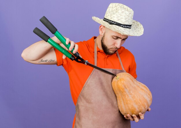 Jardinero masculino confiado con sombrero de jardinería sostiene tijeras y mira calabaza