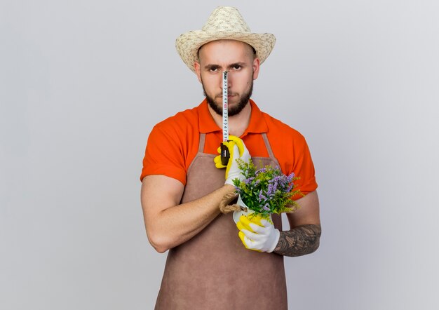 Jardinero masculino confiado con sombrero de jardinería tiene cinta métrica y maceta