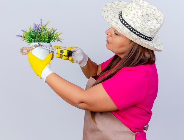 Jardinero de mediana edad mujer en delantal y sombrero con guantes de goma
