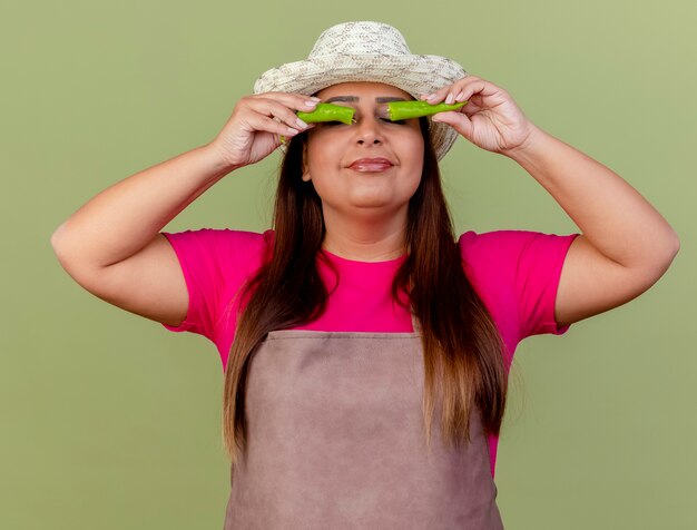 Jardinero de mediana edad mujer en delantal y sombrero sosteniendo mitades de ají verde