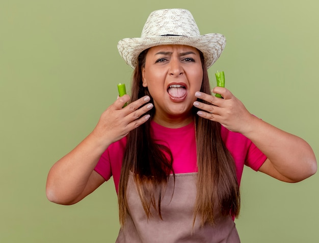 Jardinero de mediana edad mujer en delantal y sombrero sosteniendo mitades de ají verde