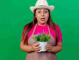 Foto gratuita jardinero de mediana edad mujer en delantal y sombrero sosteniendo planta en maceta