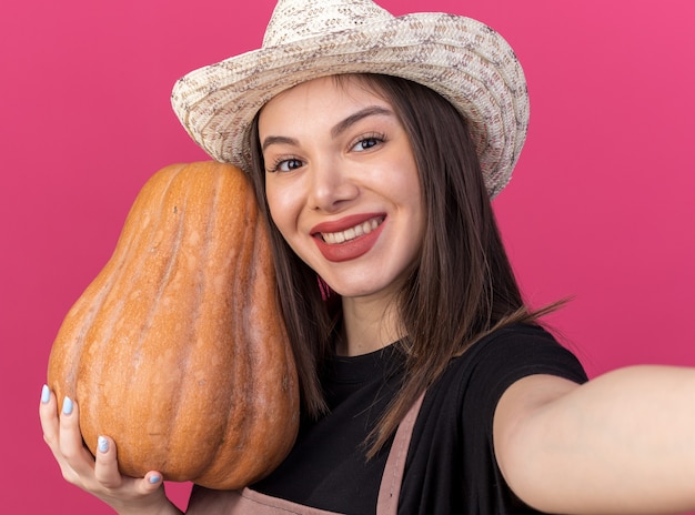 Jardinero mujer bastante caucásica sonriente vistiendo sombrero de jardinería sosteniendo calabaza y mirando a la cámara tomando selfie