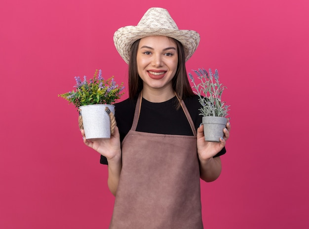 Jardinero mujer bonita caucásica sonriente vistiendo sombrero de jardinería sosteniendo macetas