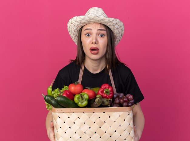 Jardinero mujer caucásica bastante ansioso vistiendo sombrero de jardinería sosteniendo canasta de verduras