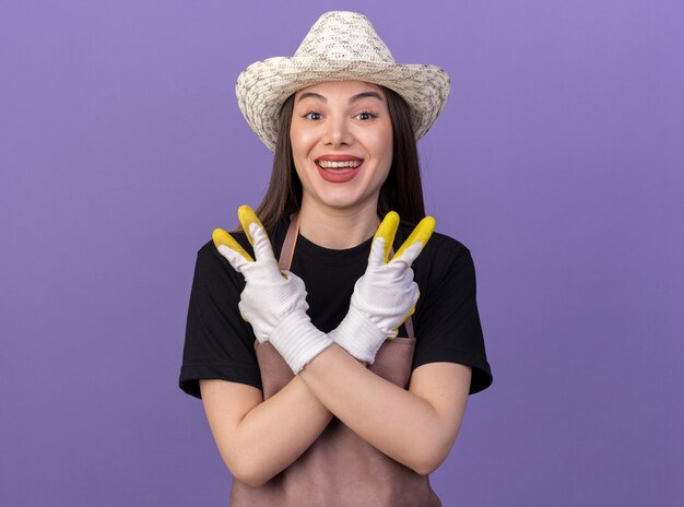 Jardinero mujer caucásica bastante feliz vistiendo guantes y sombrero de jardinería gesticulando el signo de la victoria