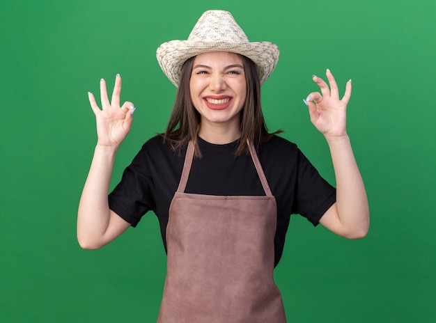 Jardinero mujer caucásica bastante sonriente con sombrero de jardinería gesticulando bien firmar con las dos manos