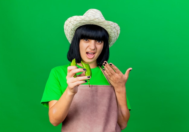 Jardinero mujer joven molesto en uniforme vistiendo sombrero de jardinería tiene pimienta rota