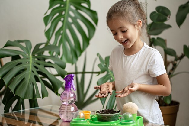 Jardinero de niña divertida con plantas en la habitación en casa, regando y cuidando plantas de interior, trasplanta flores.