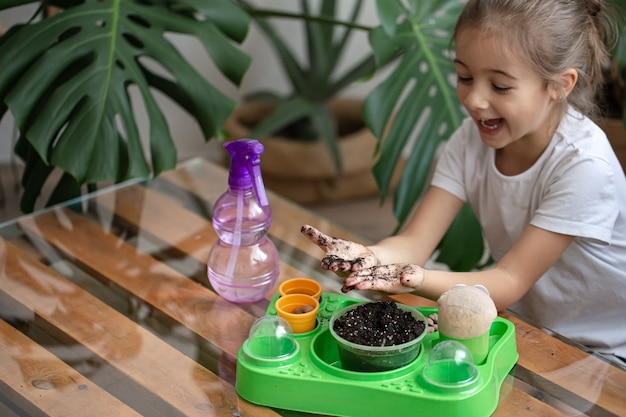 Jardinero de niña divertida con plantas en la habitación en casa, regando y cuidando plantas de interior, trasplanta flores.