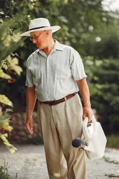 Jardinero senior disfruta de su trabajo en el jardín. Anciano con camisa blanca.