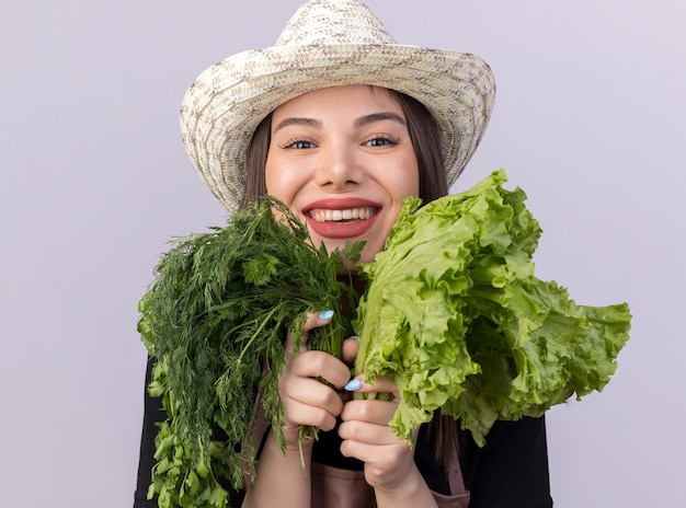 Jardinero de sexo femenino bastante caucásico sonriente que lleva el sombrero que cultiva un huerto que sostiene el manojo de eneldo y ensalada