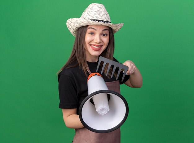 Jardinero de sexo femenino bastante caucásico sonriente que lleva el sombrero que cultiva un huerto que sostiene el rastrillo y el altavoz fuerte