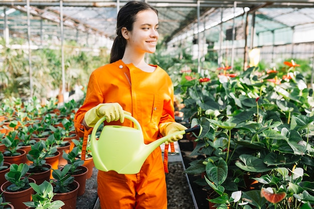 Jardinero de sexo femenino feliz que sostiene la regadera en invernadero