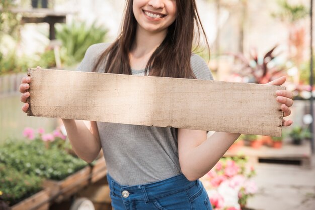 Jardinero de sexo femenino feliz que sostiene el tablón de madera