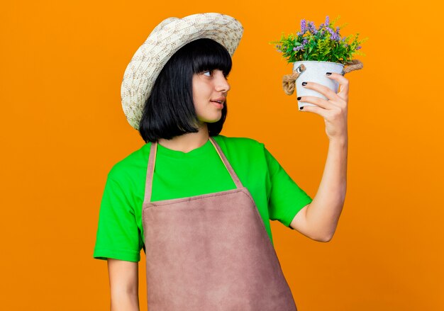 Foto gratuita jardinero de sexo femenino joven emocionado en uniforme vistiendo sombrero de jardinería sostiene maceta