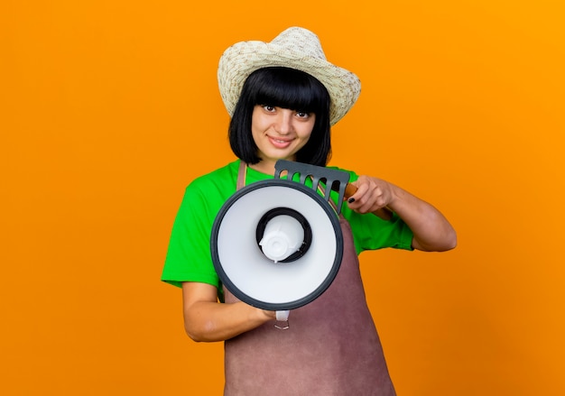 Jardinero de sexo femenino joven sonriente en uniforme vistiendo sombrero de jardinería tiene altavoz