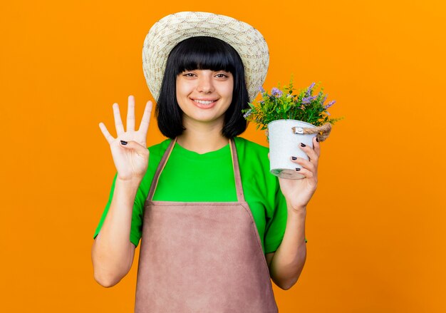 Jardinero de sexo femenino joven sonriente en uniforme vistiendo sombrero de jardinería tiene maceta