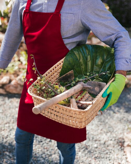 Un jardinero de sexo femenino que sostiene la cesta con la azada y la ramita cosechada