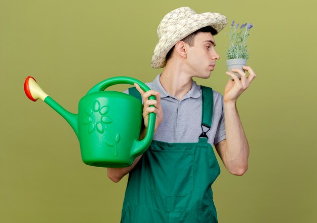 Jardinero de sexo masculino joven confiado con sombrero de jardinería sosteniendo y oliendo flores