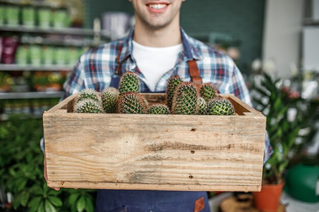 Jardinero smiing feliz sosteniendo una olla con cactus en una tienda de flores