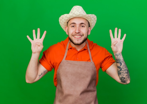 Foto gratuita jardinero sonriente hombre vestido con sombrero de jardinería gestos ocho con los dedos
