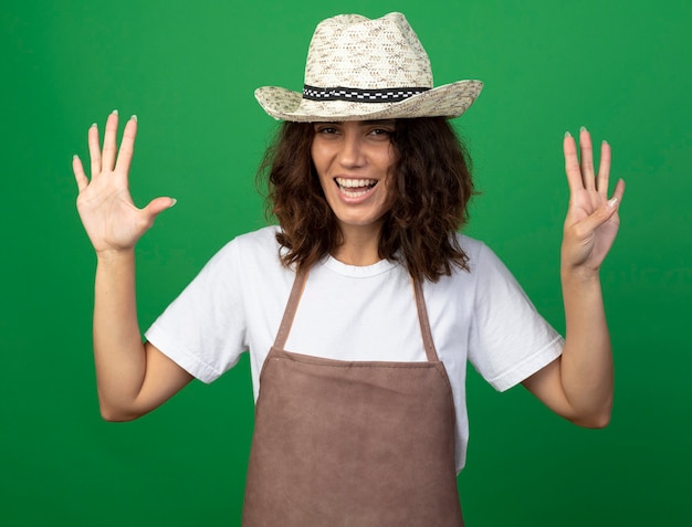 Jardinero sonriente joven en uniforme con sombrero de jardinería mostrando diferentes números aislados en verde