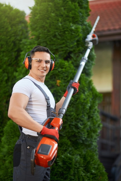 Jardinero sonriente sosteniendo cortasetos de gasolina al aire libre