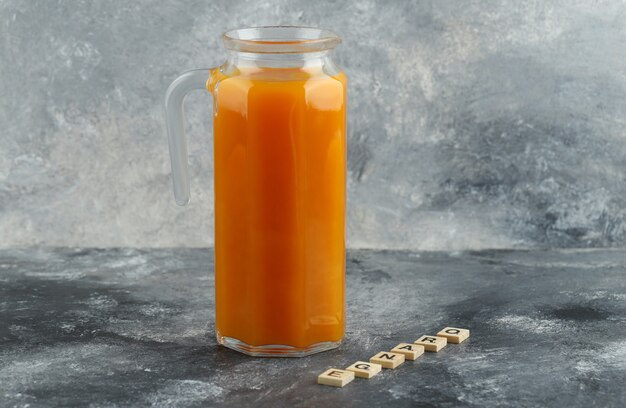 Jarra de jugo de naranja con letras de madera sobre mesa de mármol.