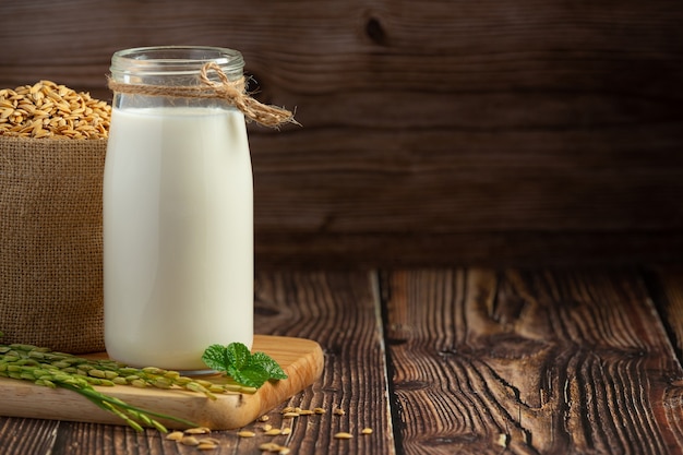 Jarra de leche de arroz con planta de arroz y semilla de arroz puesta sobre un piso de madera