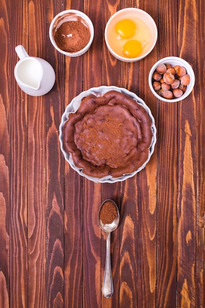 Foto gratuita jarra de leche; café en polvo de chocolate; yema de huevo y avellana para hacer pastel fresco en superficie de madera