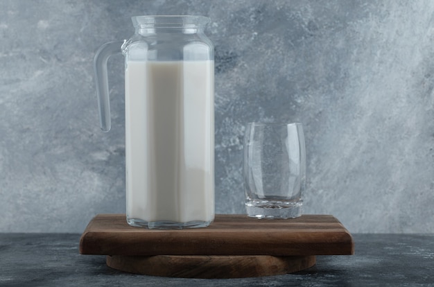 Jarra de leche fresca y vaso de agua sobre tabla de madera.